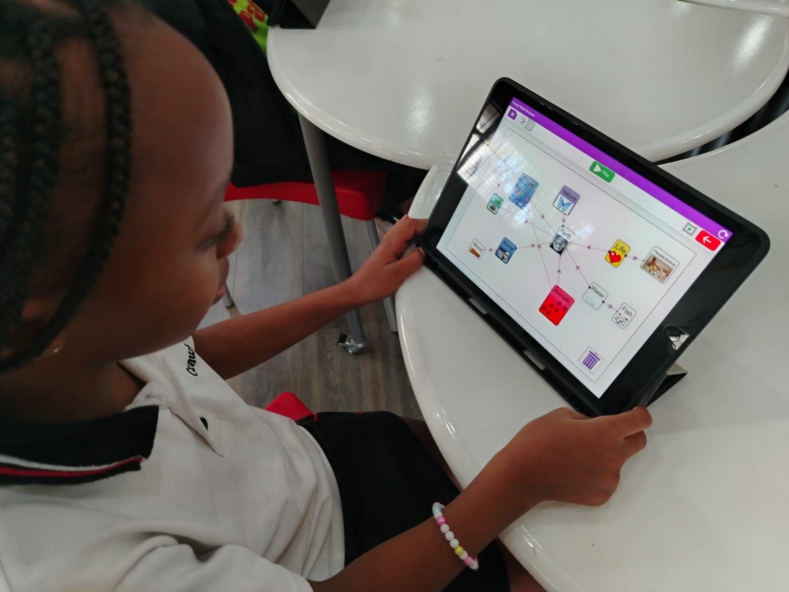 A young girl is sitting at a table using a tablet computer