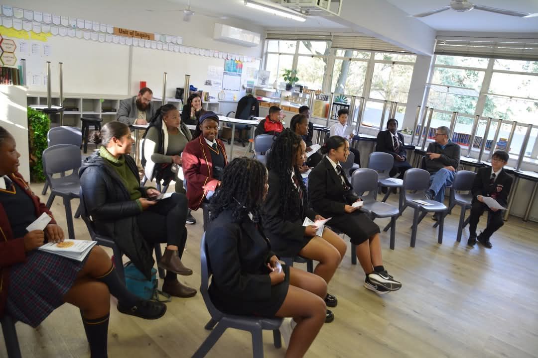 People seated in a room, likely a school, some holding papers.
