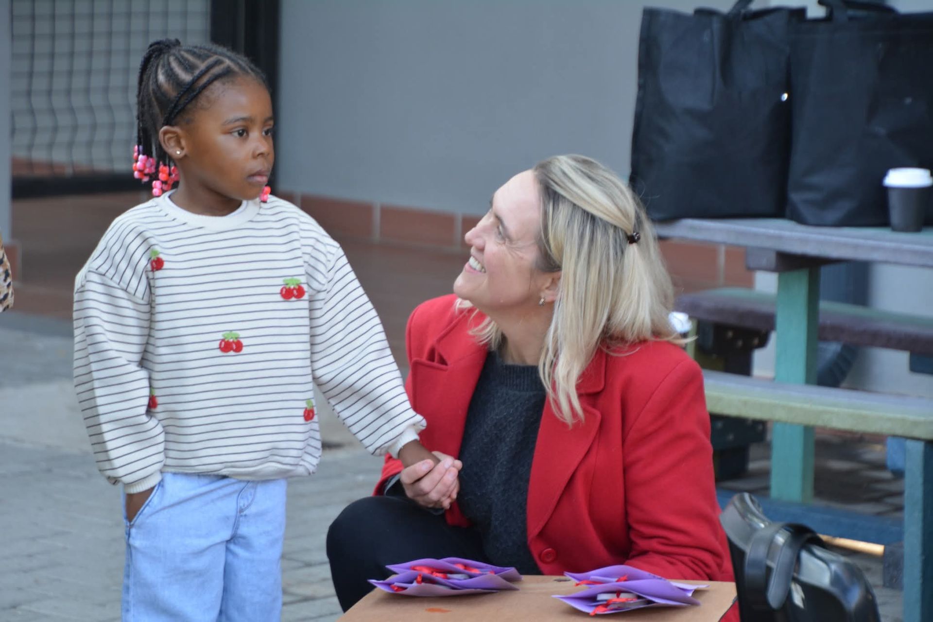Woman in red jacket holds hands with child wearing sweater with cherry design.