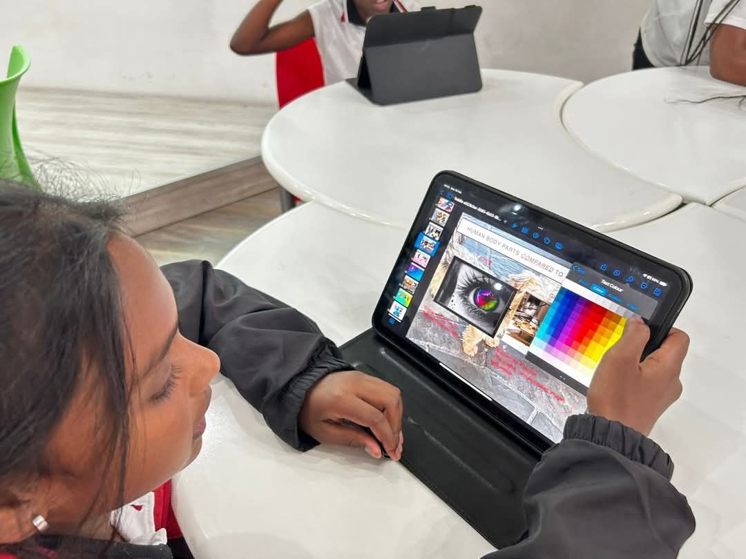 Girl using a tablet at a white table, drawing on a digital art program with a color palette visible.
