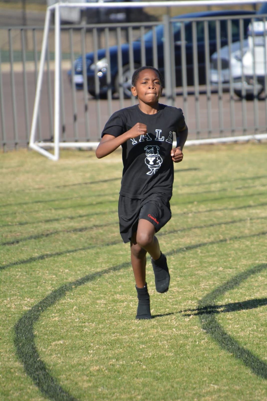 Boy running on a track, wearing black shirt and shorts.