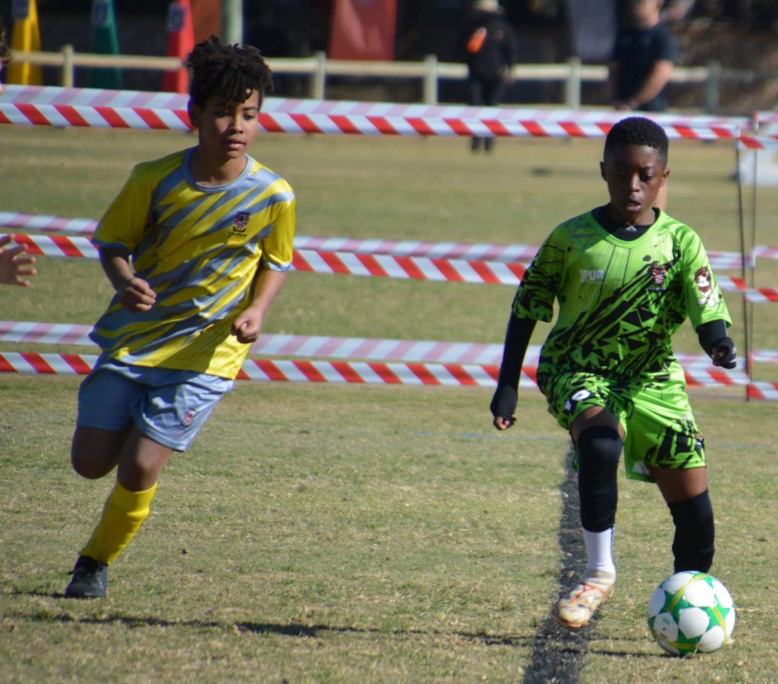 Two soccer players on a grass field: one in yellow, one in green, with the ball.