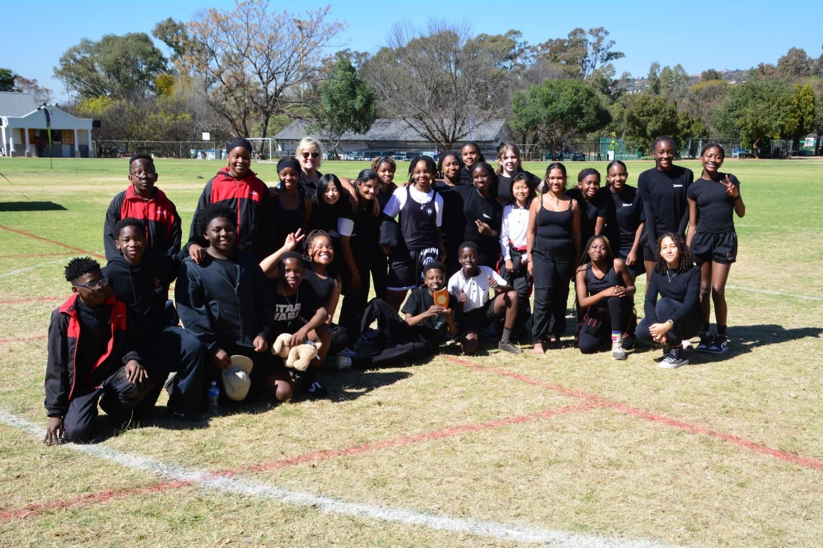 Group of students posing on a grassy field, wearing mostly black clothing, smiling.