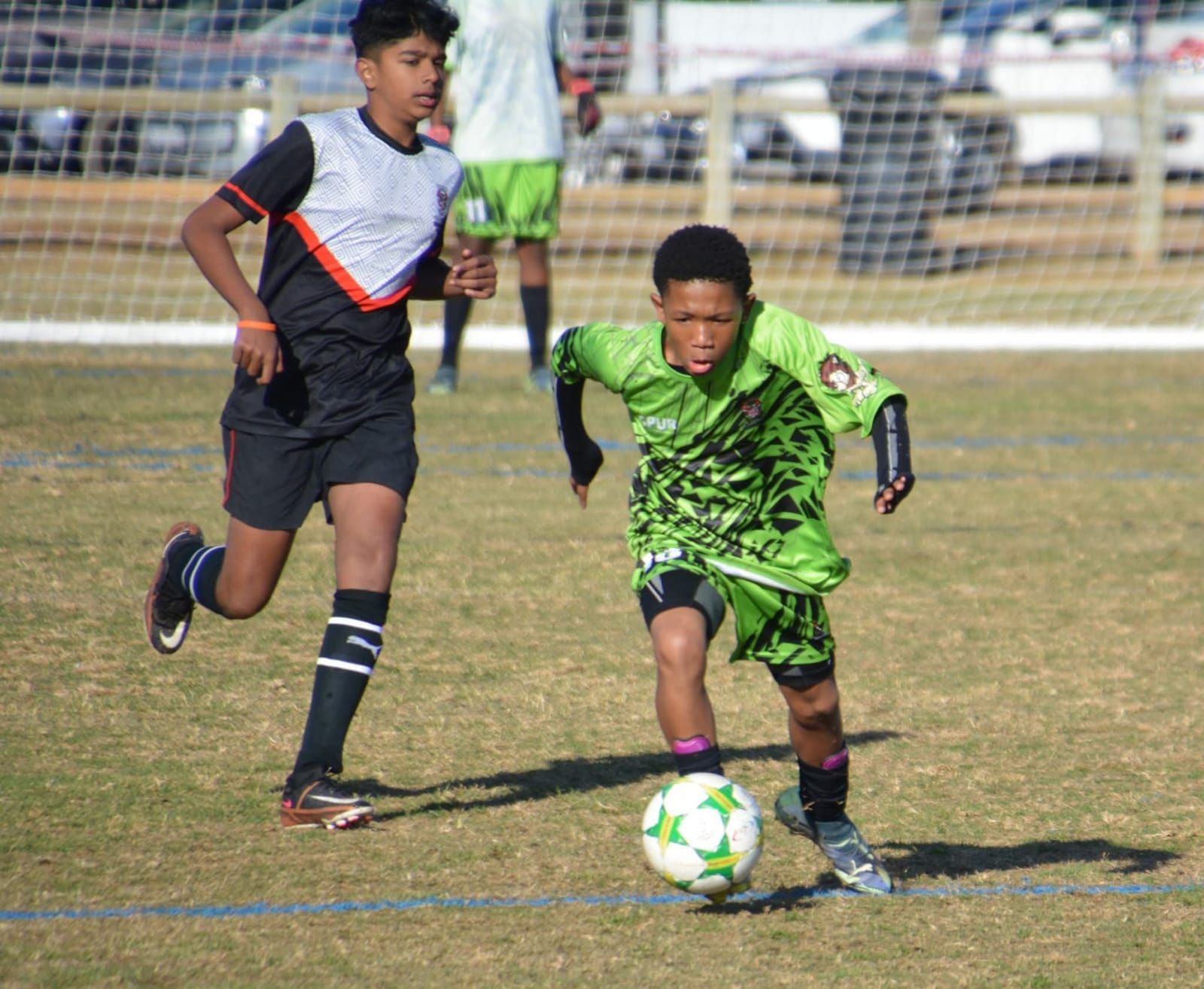 Two soccer players on a green field: one in black, the other in green dribbling the ball.