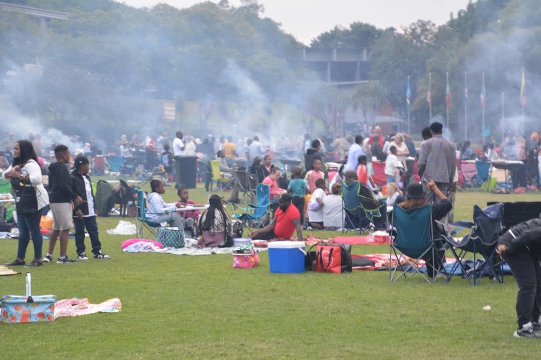 Large crowd picnicking in a grassy park, visible smoke, people sitting in chairs and blankets.