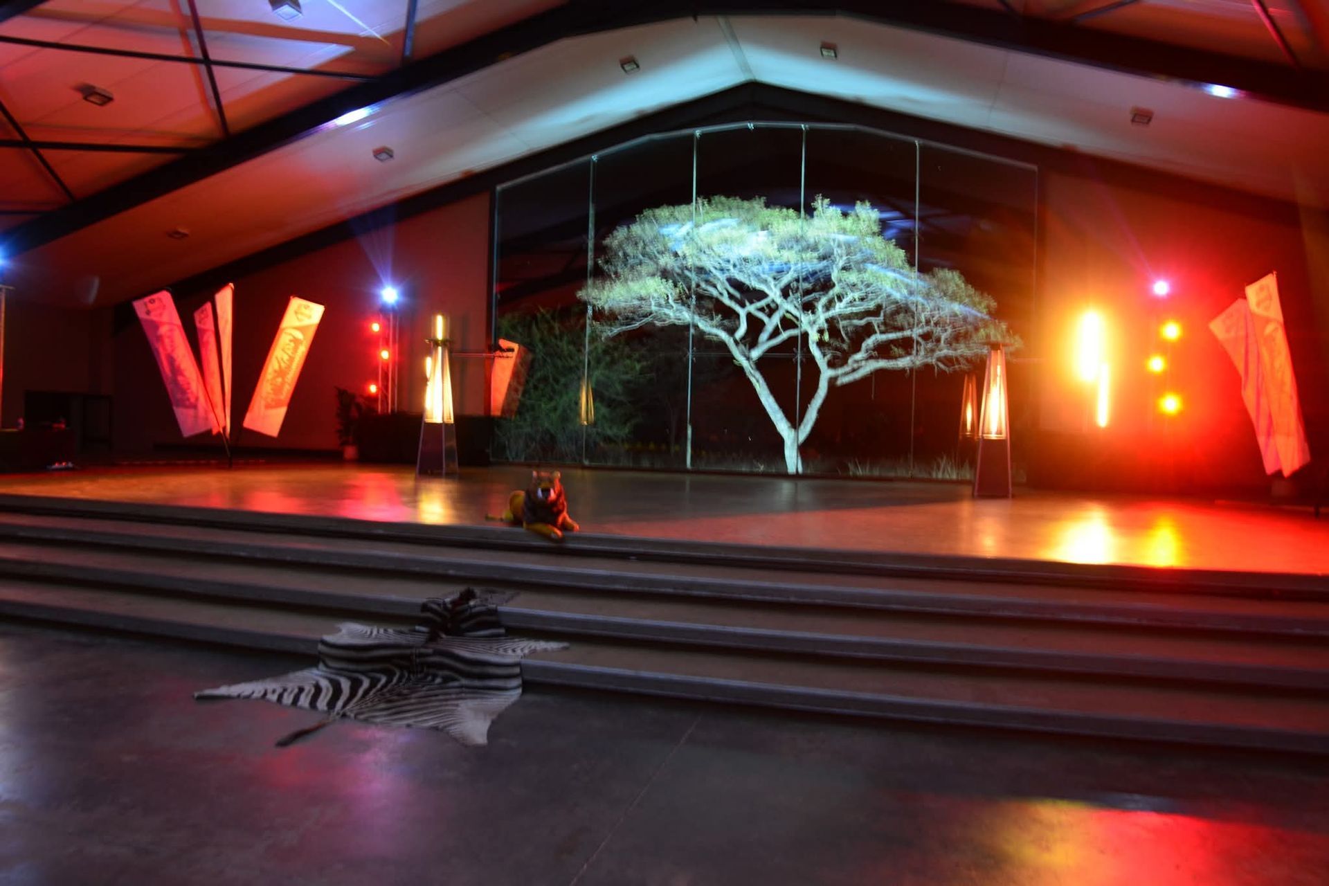 Stage with illuminated tree backdrop, zebra skin rug, and colorful lighting.