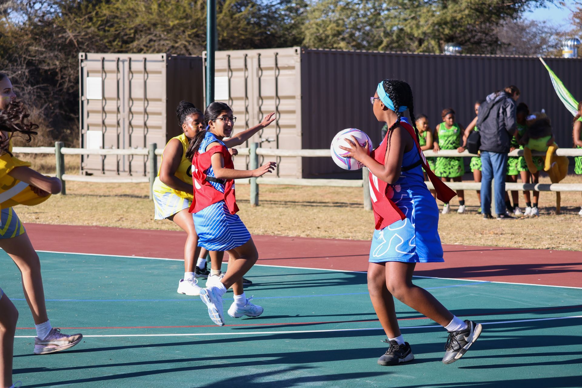 Netball players in blue and red uniforms on a court, one with ball.