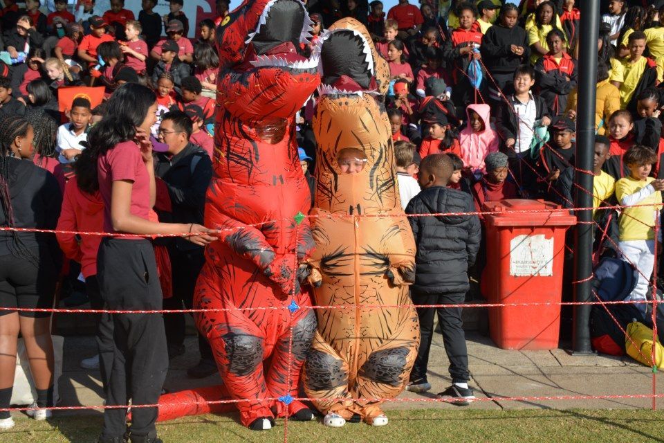 Two people in dinosaur costumes are standing next to each other in front of a crowd.