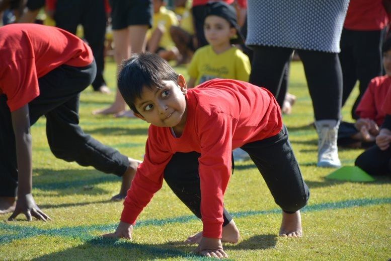 A young boy in a red shirt is crawling on the grass.