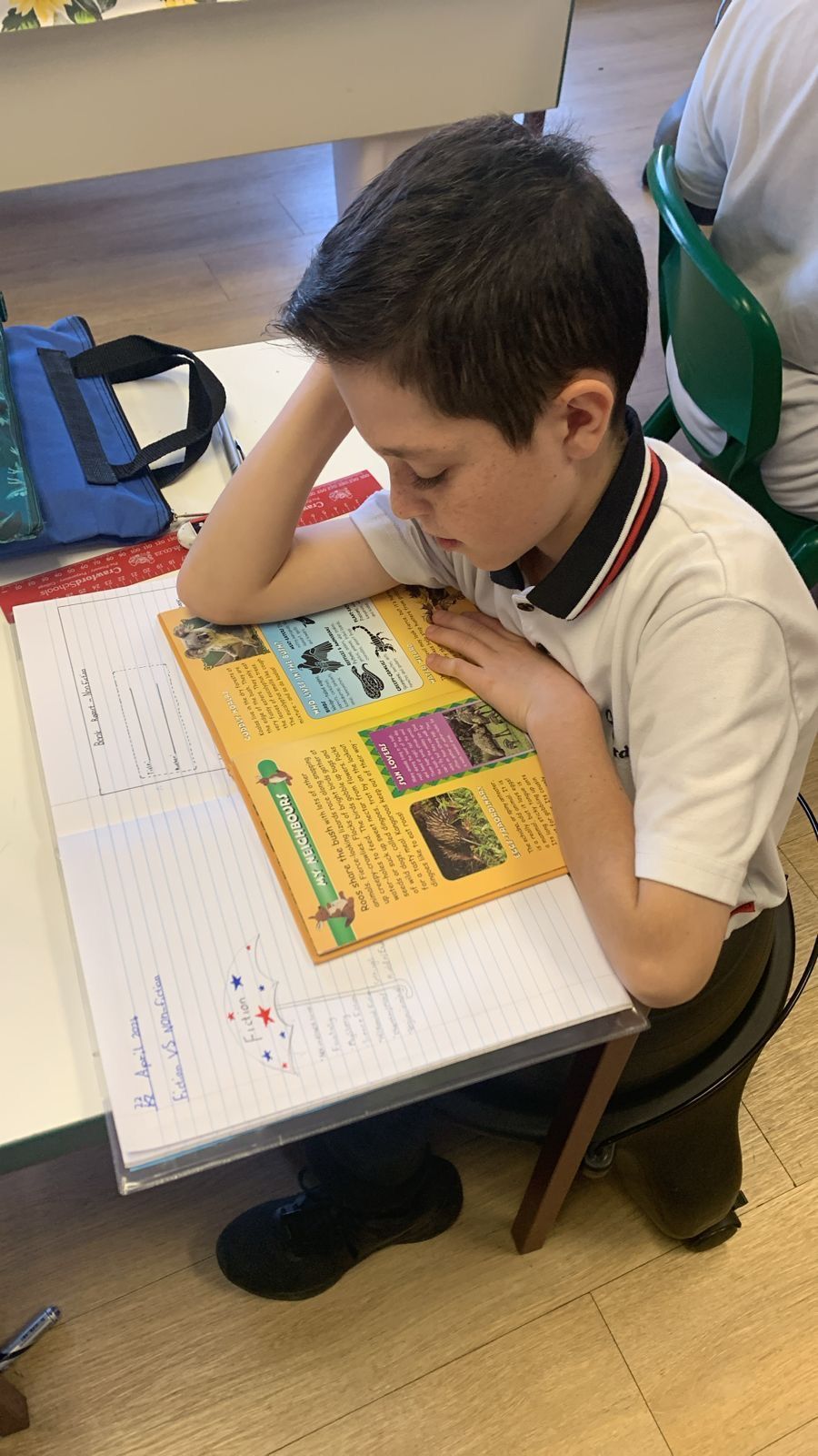 A young boy is sitting at a desk reading a book.