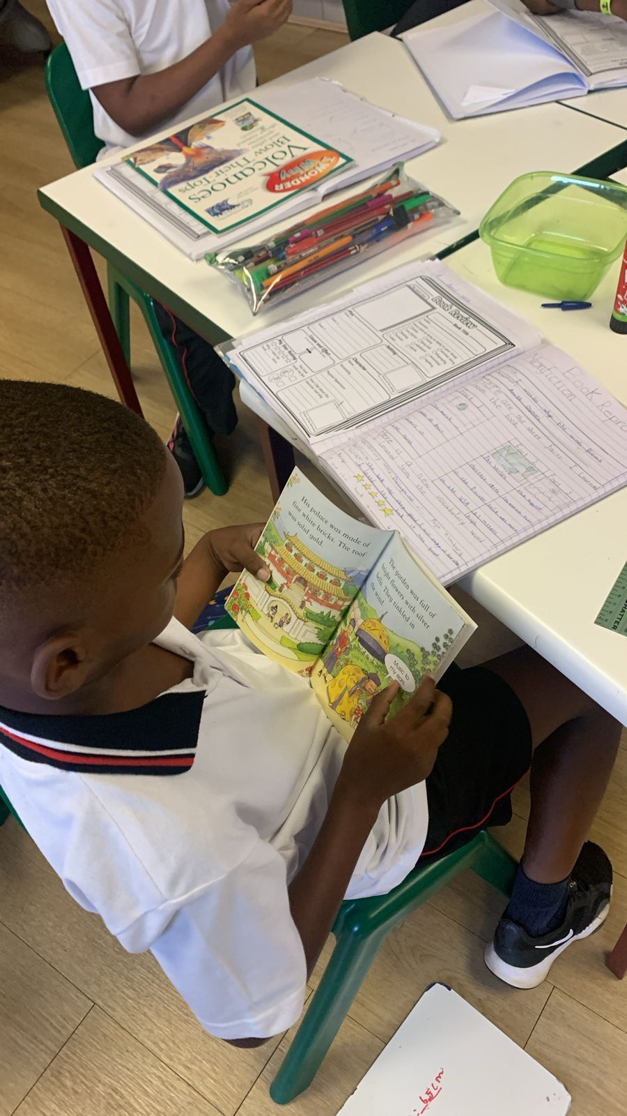 A young boy is sitting at a table reading a book.