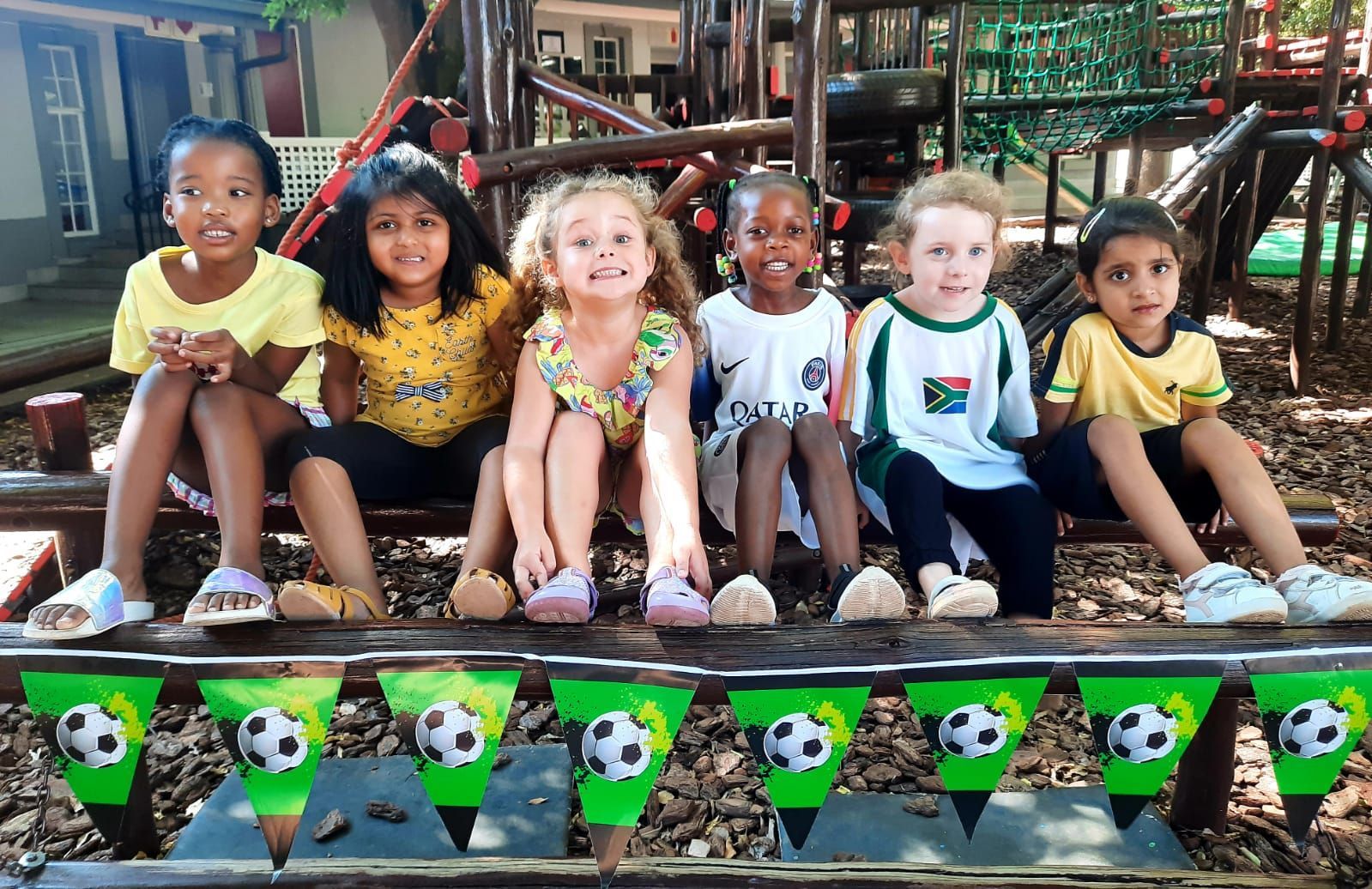 A group of children are sitting on a bench with soccer flags.