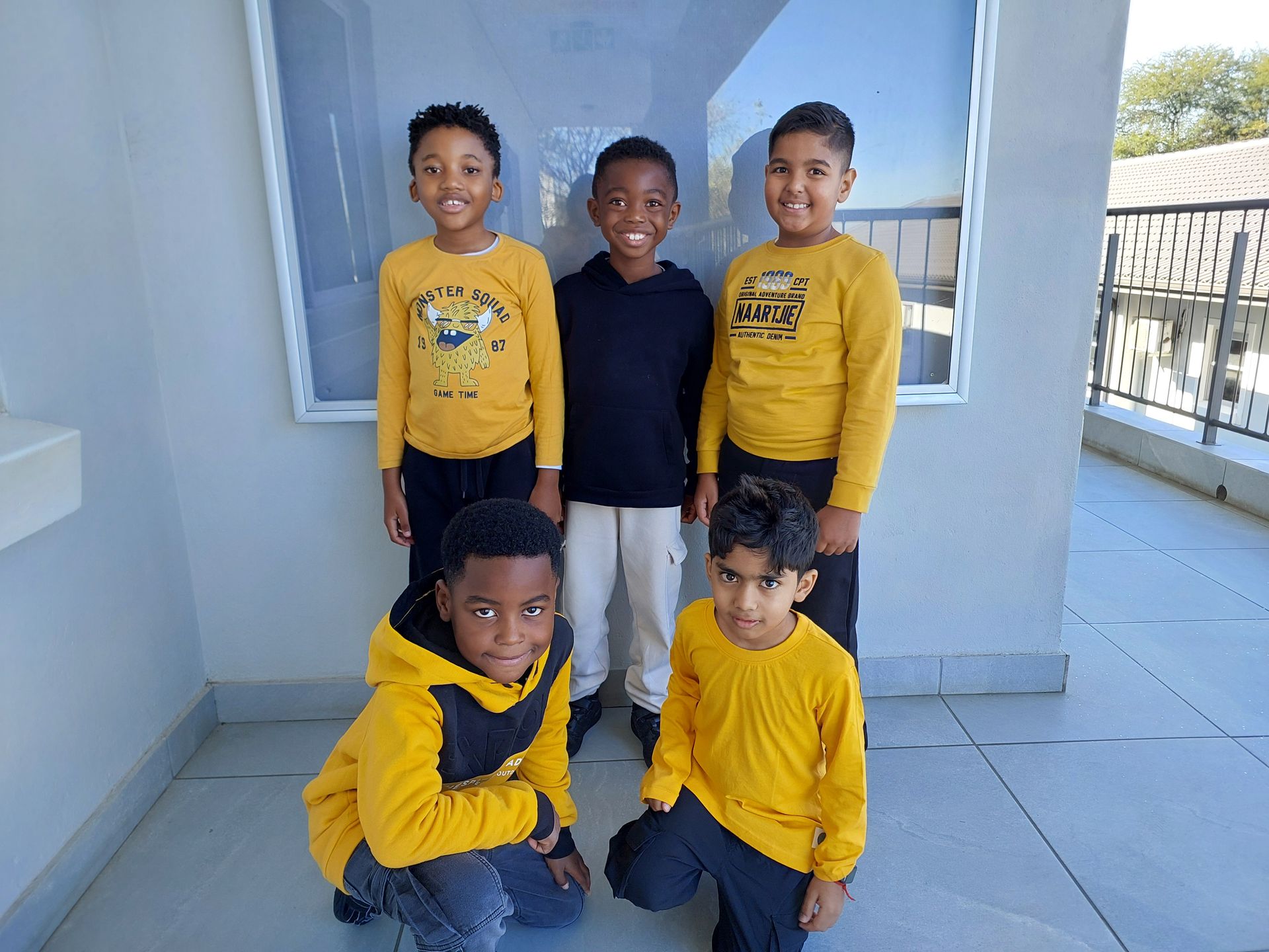 Five children standing and kneeling outside, wearing yellow and black shirts.