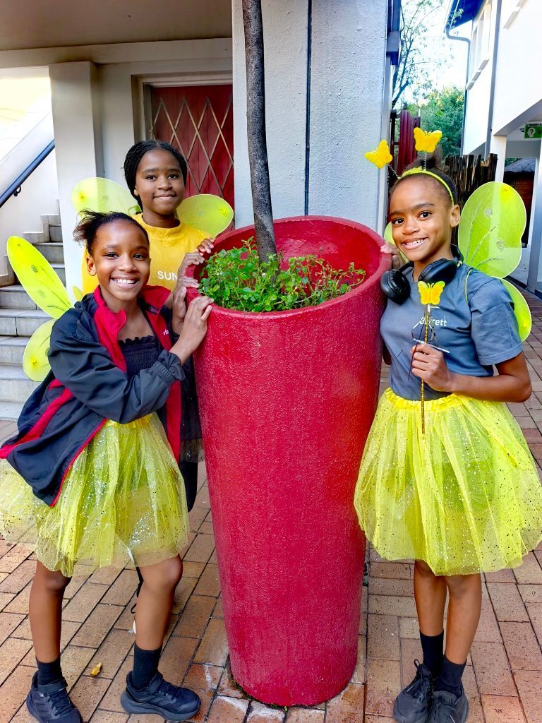 Three children in fairy costumes pose by a red planter.