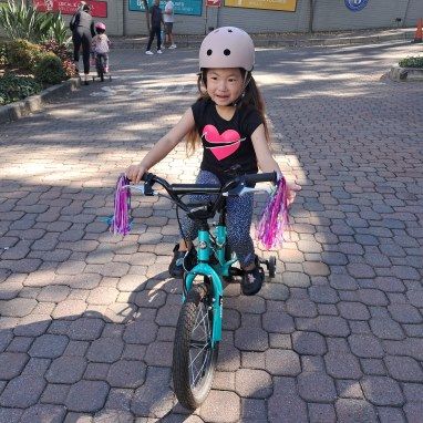 A little girl is riding a bike on a brick sidewalk.