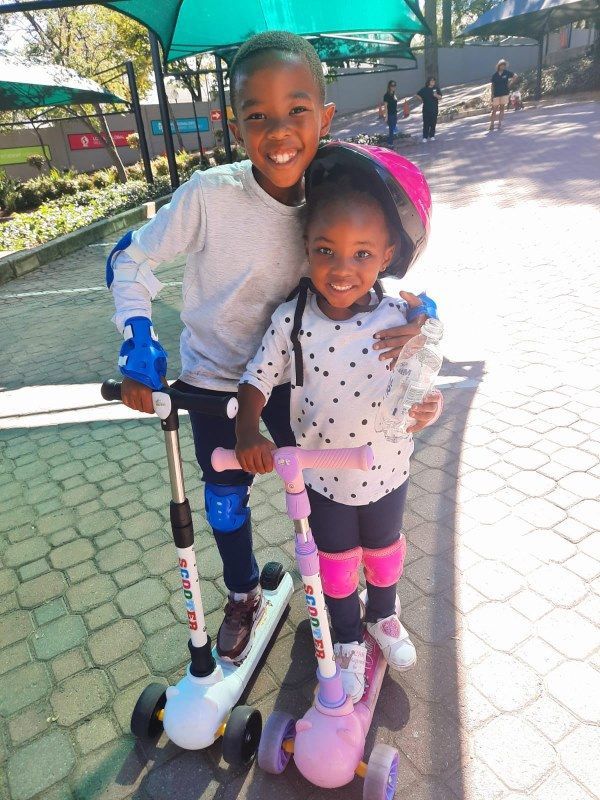 A boy and a girl are standing next to each other on scooters.
