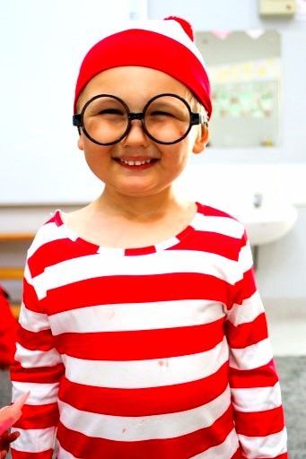 Child in red and white striped shirt, hat, and round glasses smiles.
