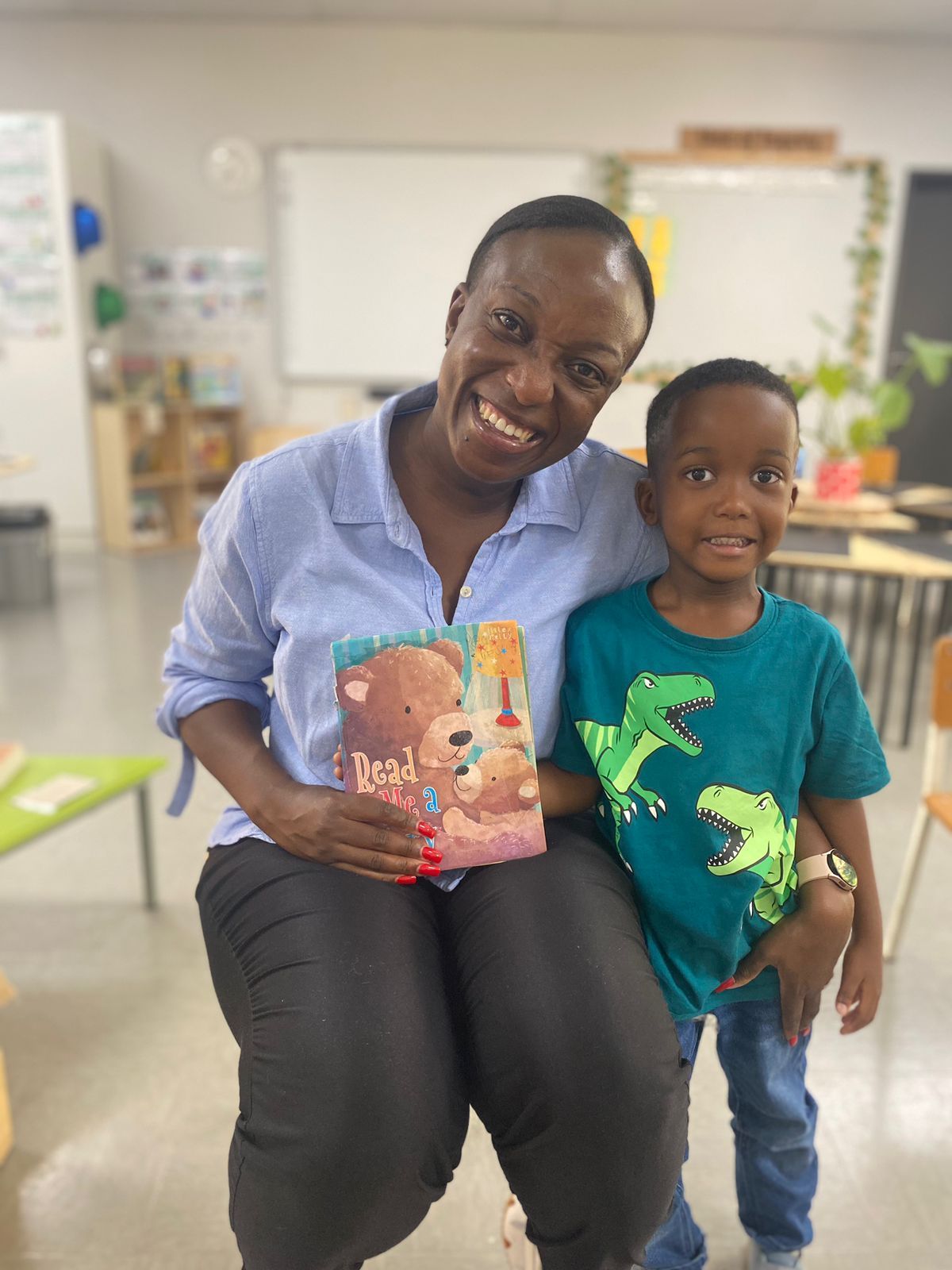 A woman is sitting next to a young boy in a classroom holding a book.