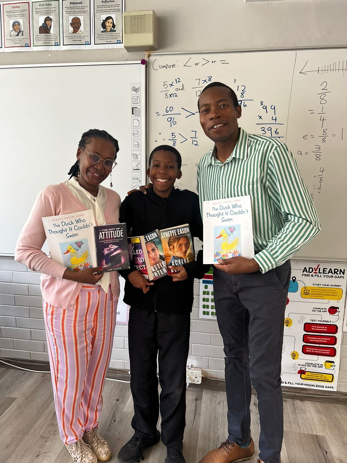 Three people are standing next to each other in a classroom holding books.