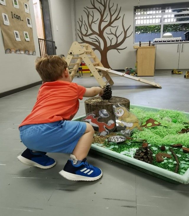 A young boy is squatting down in front of a sensory table