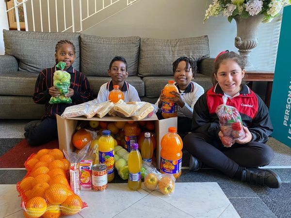 A group of children are sitting on the floor holding bags of fruit.