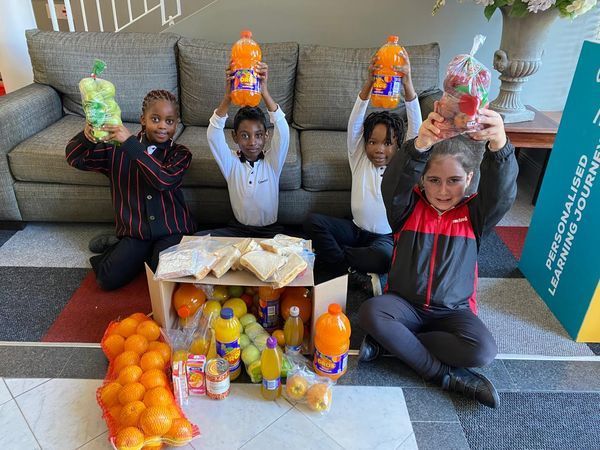 A group of children are sitting on the floor holding up bottles of orange juice.