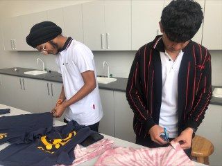 Two young men are cutting shirts in a kitchen.