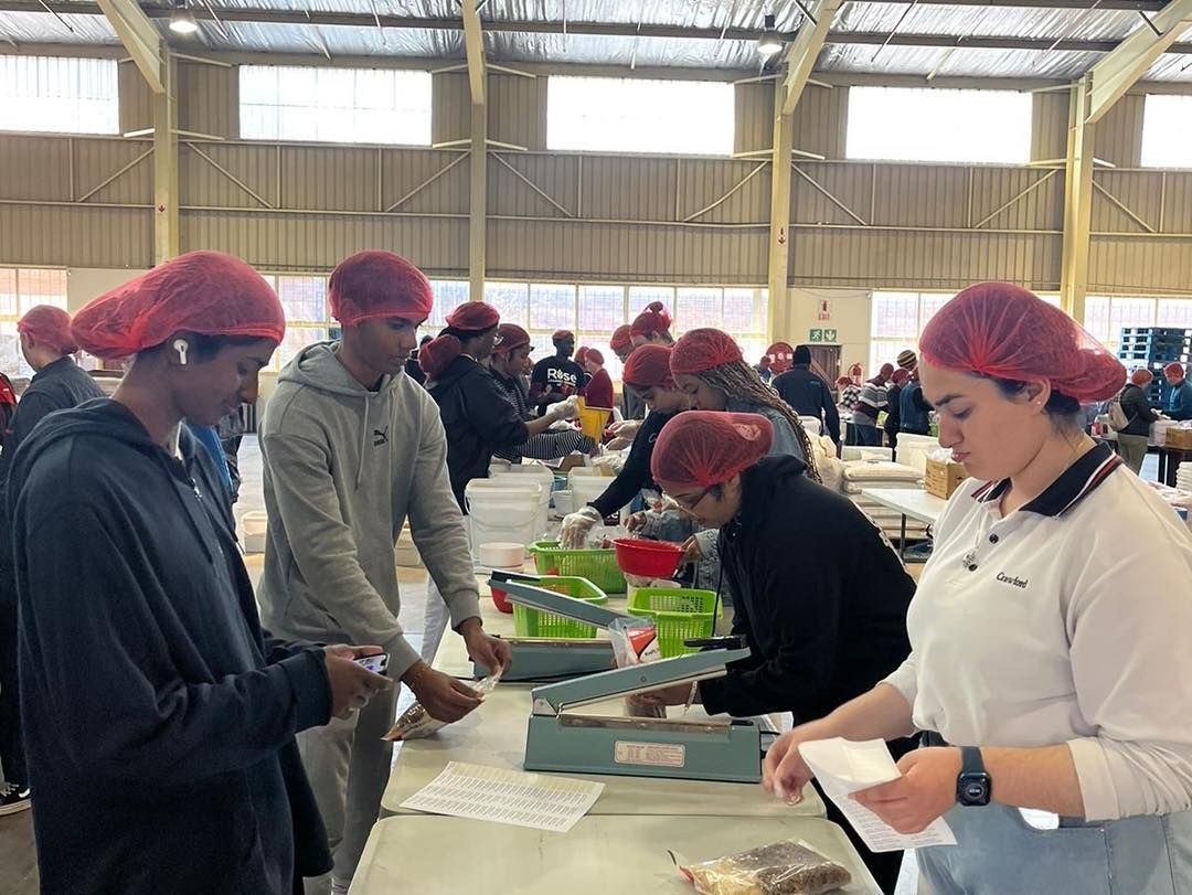 A group of people wearing red hair nets are working in a kitchen.