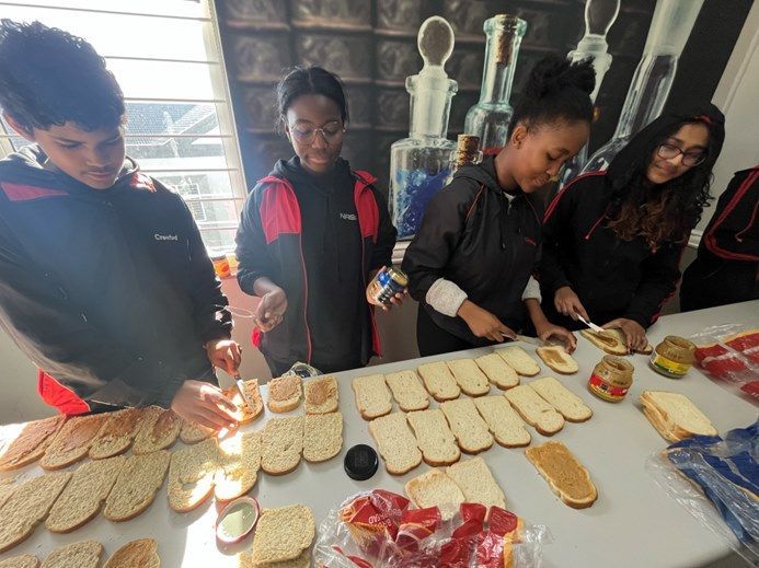 A group of young people are making sandwiches on a table.