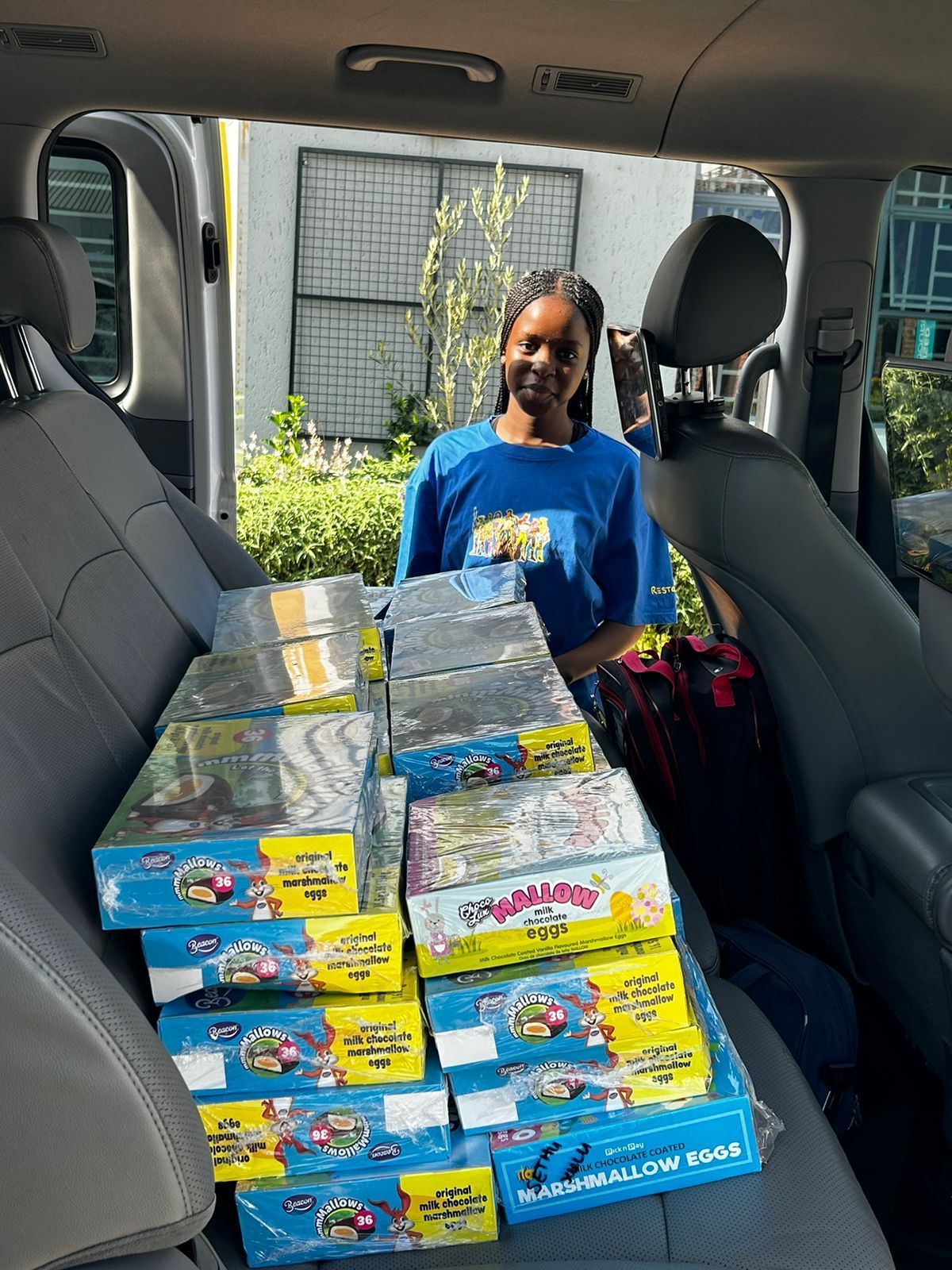 A woman is standing in the back seat of a car filled with boxes.