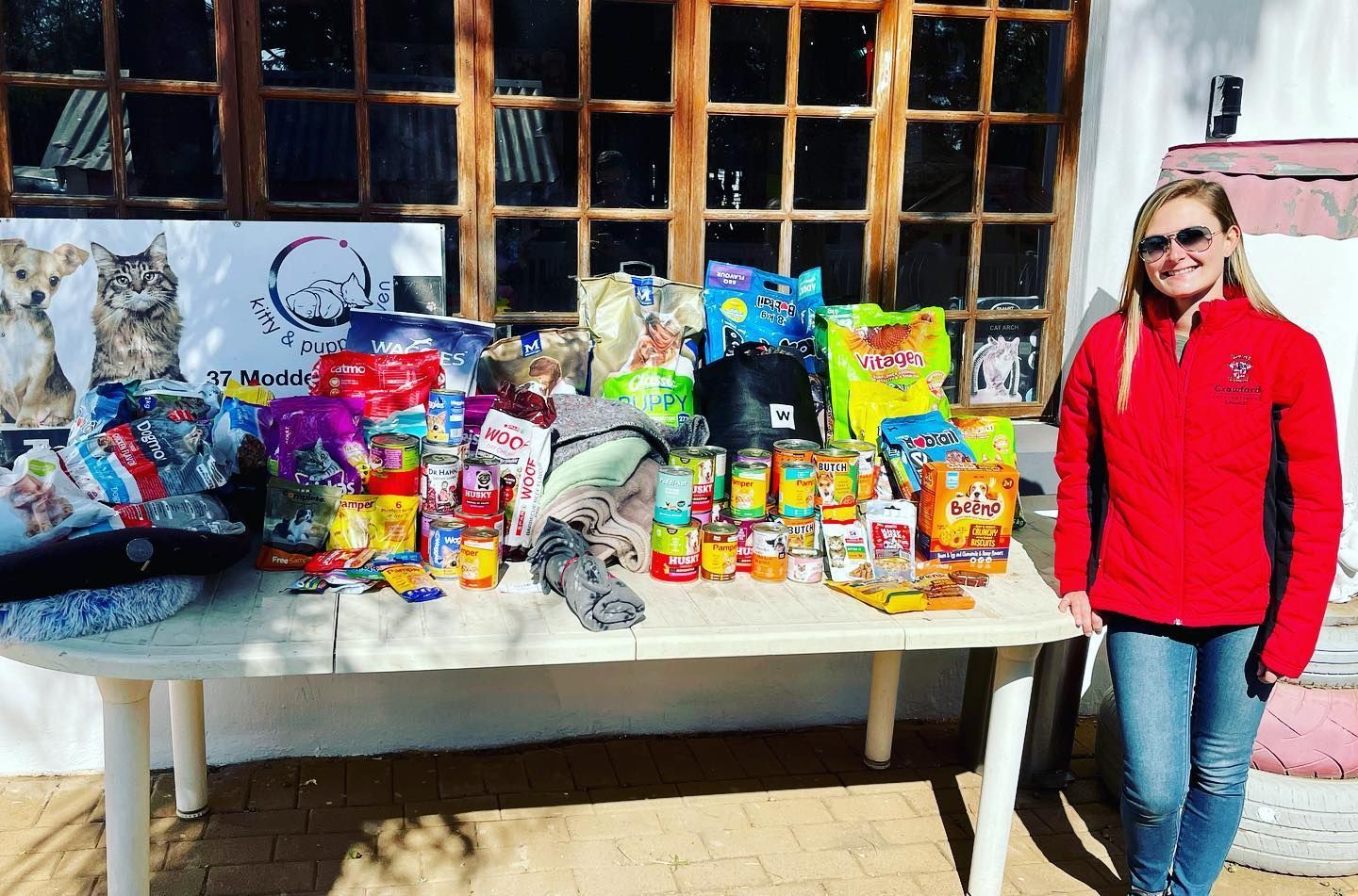 A woman in a red jacket is standing in front of a table filled with dog food.