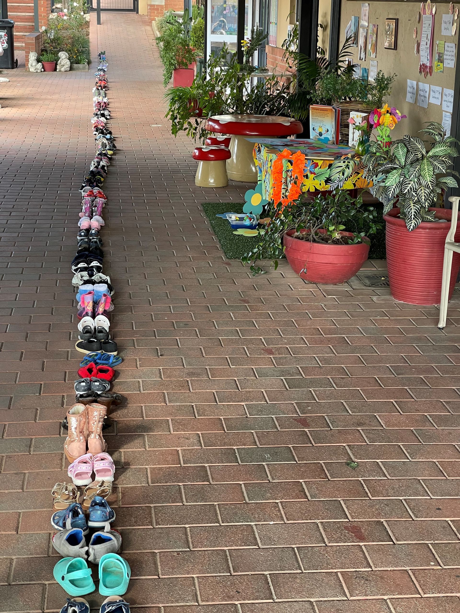 A row of shoes are lined up on a brick sidewalk.
