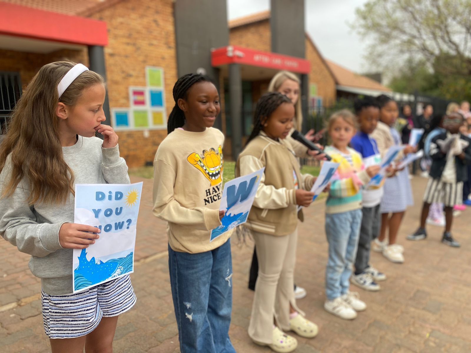 A group of children are standing in front of a building holding signs.
