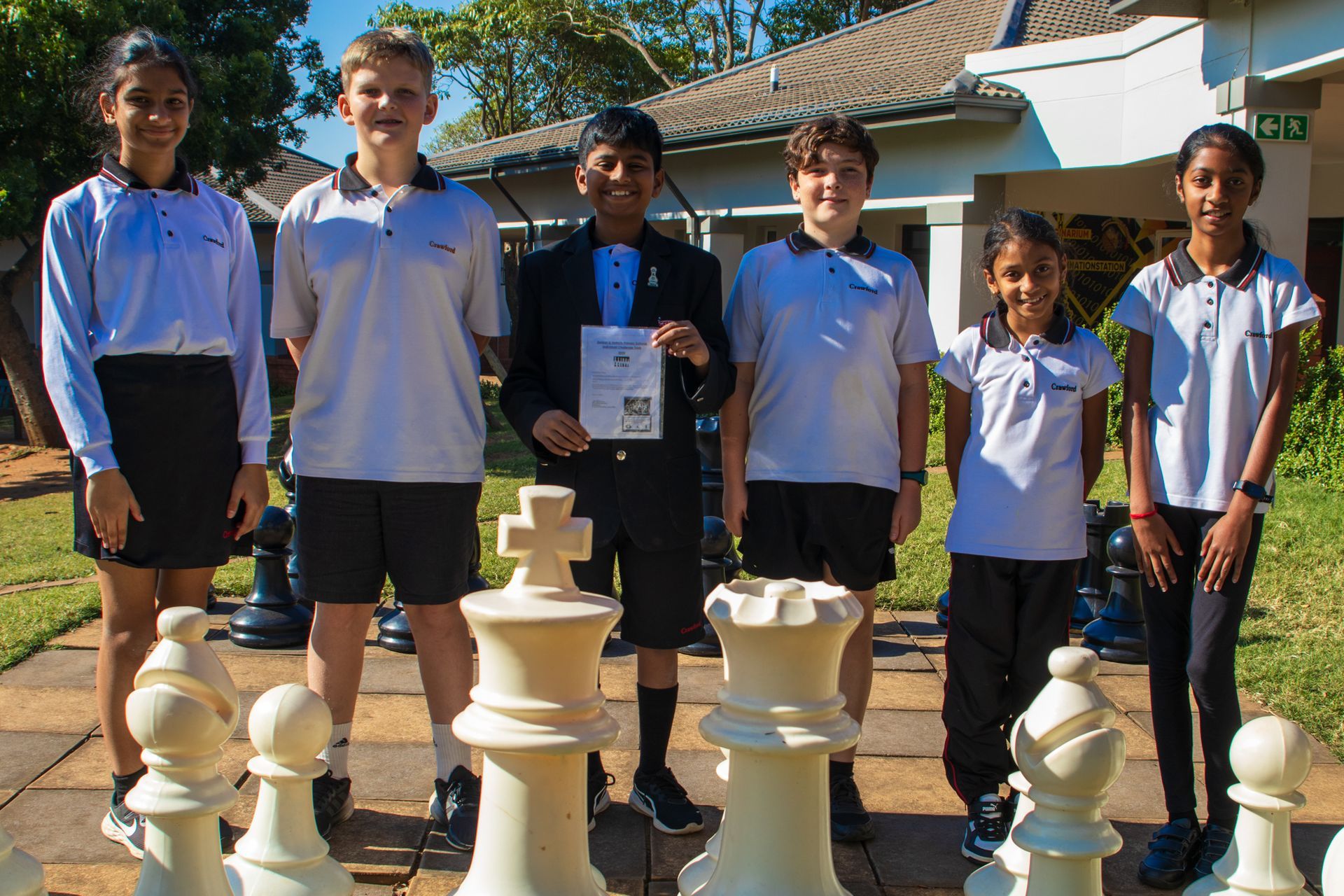 A group of children are standing next to giant chess pieces.