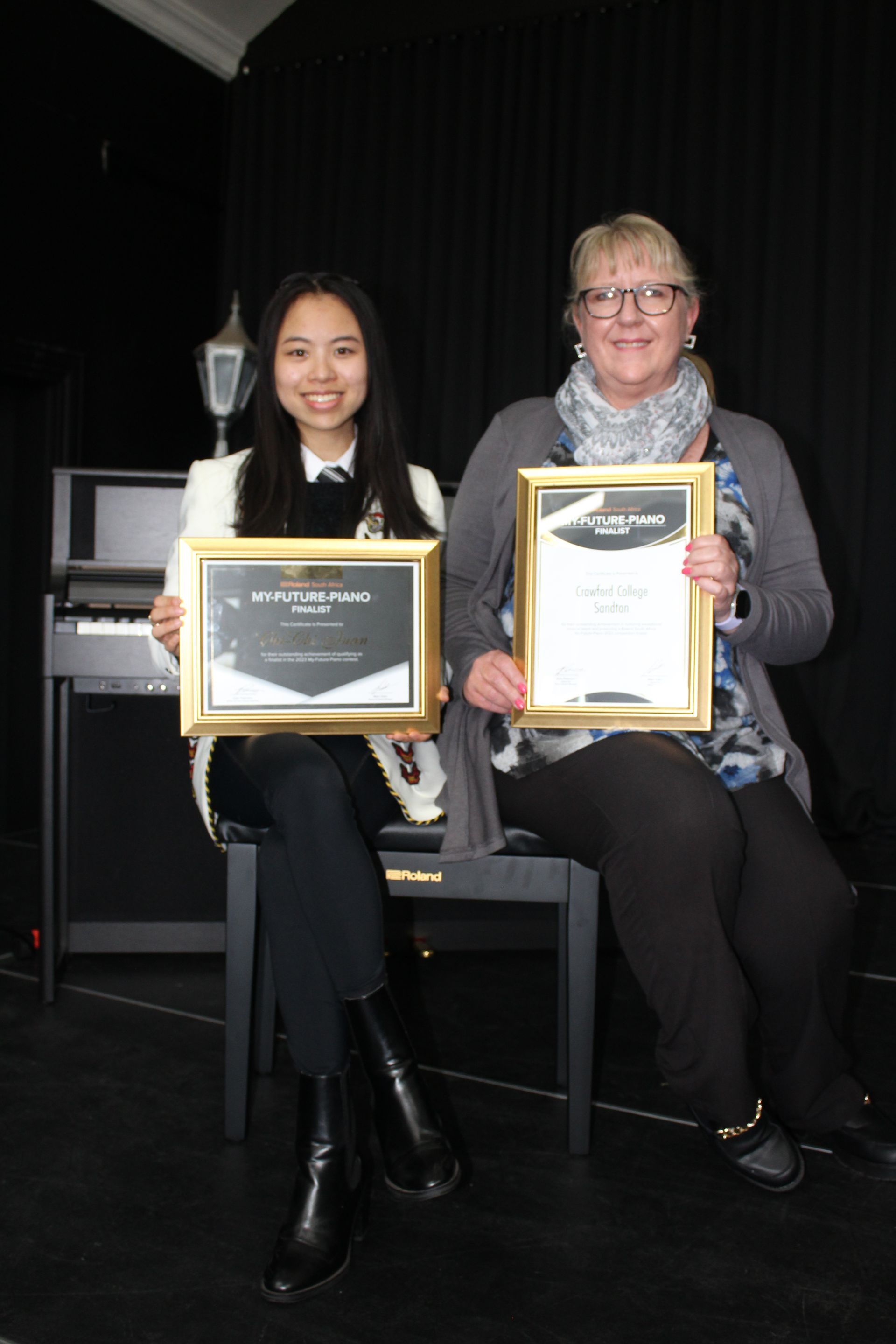 Two women are sitting next to each other holding certificates.