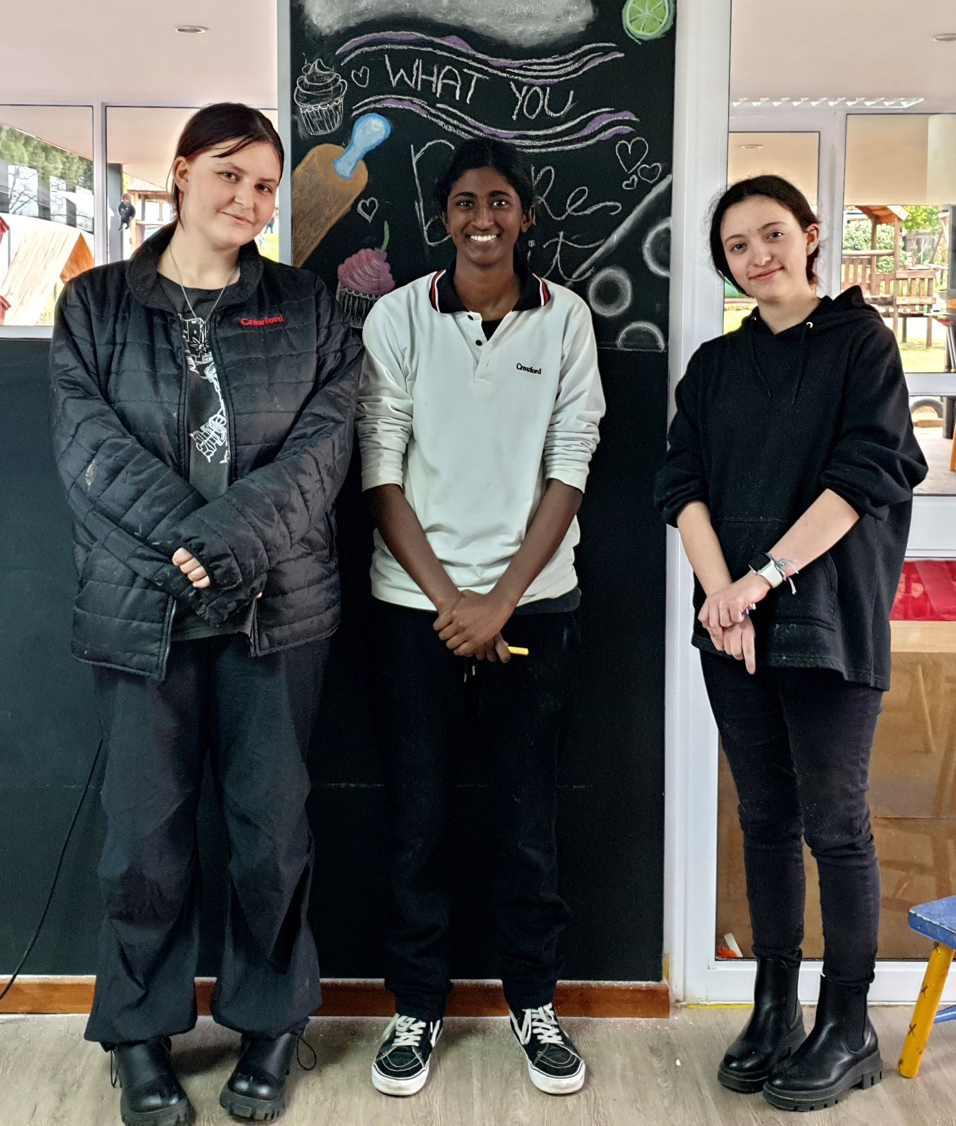 Three women are posing for a picture in front of a chalkboard.