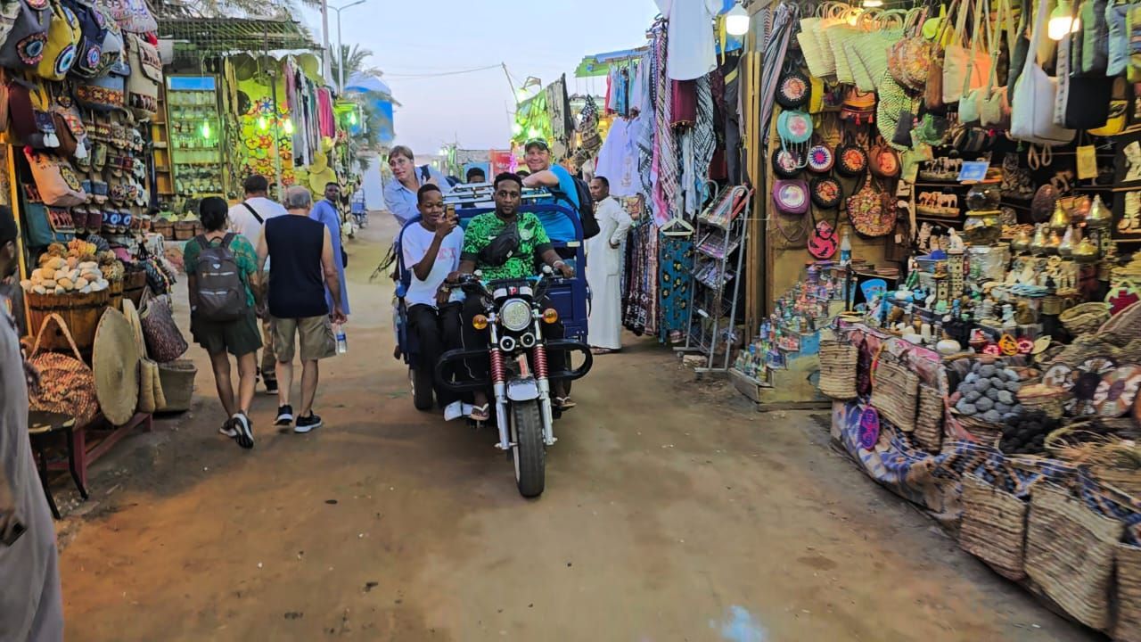 A man is riding a motorcycle down a dirt road in a market.