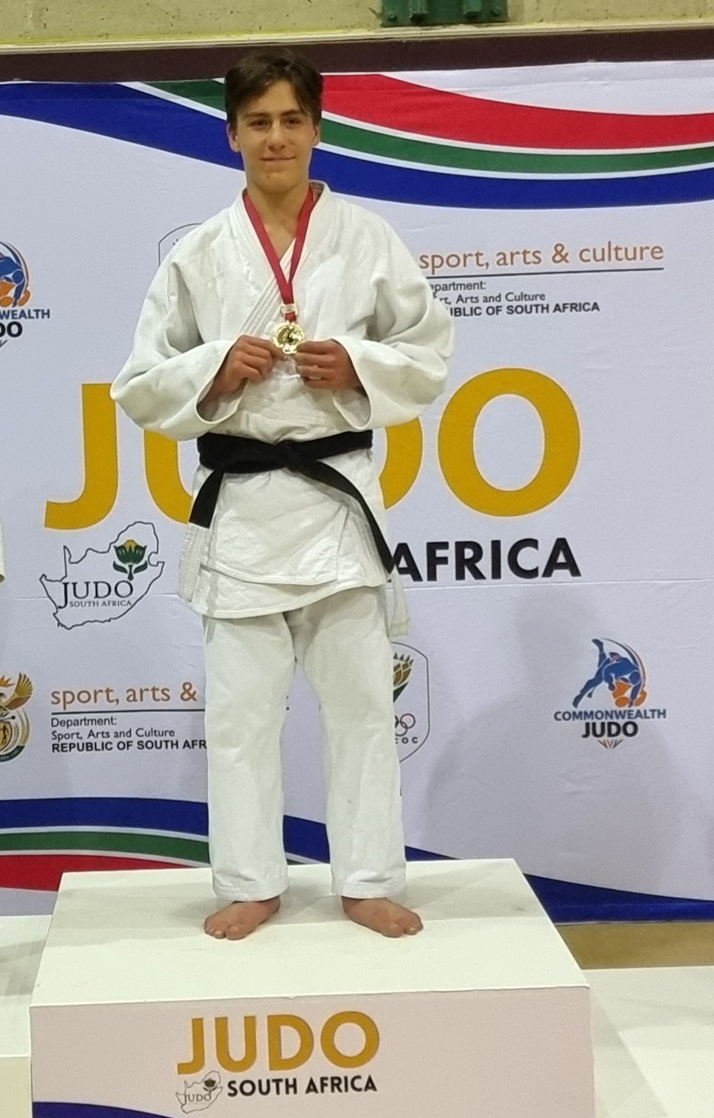 A young man in a judo uniform is standing on a podium holding a medal.