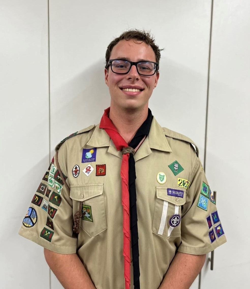 A boy scout wearing glasses and a tie is smiling for the camera