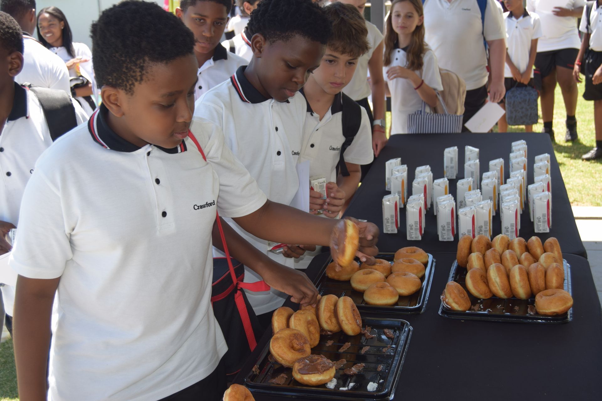 A group of children are standing around a table with donuts and drinks