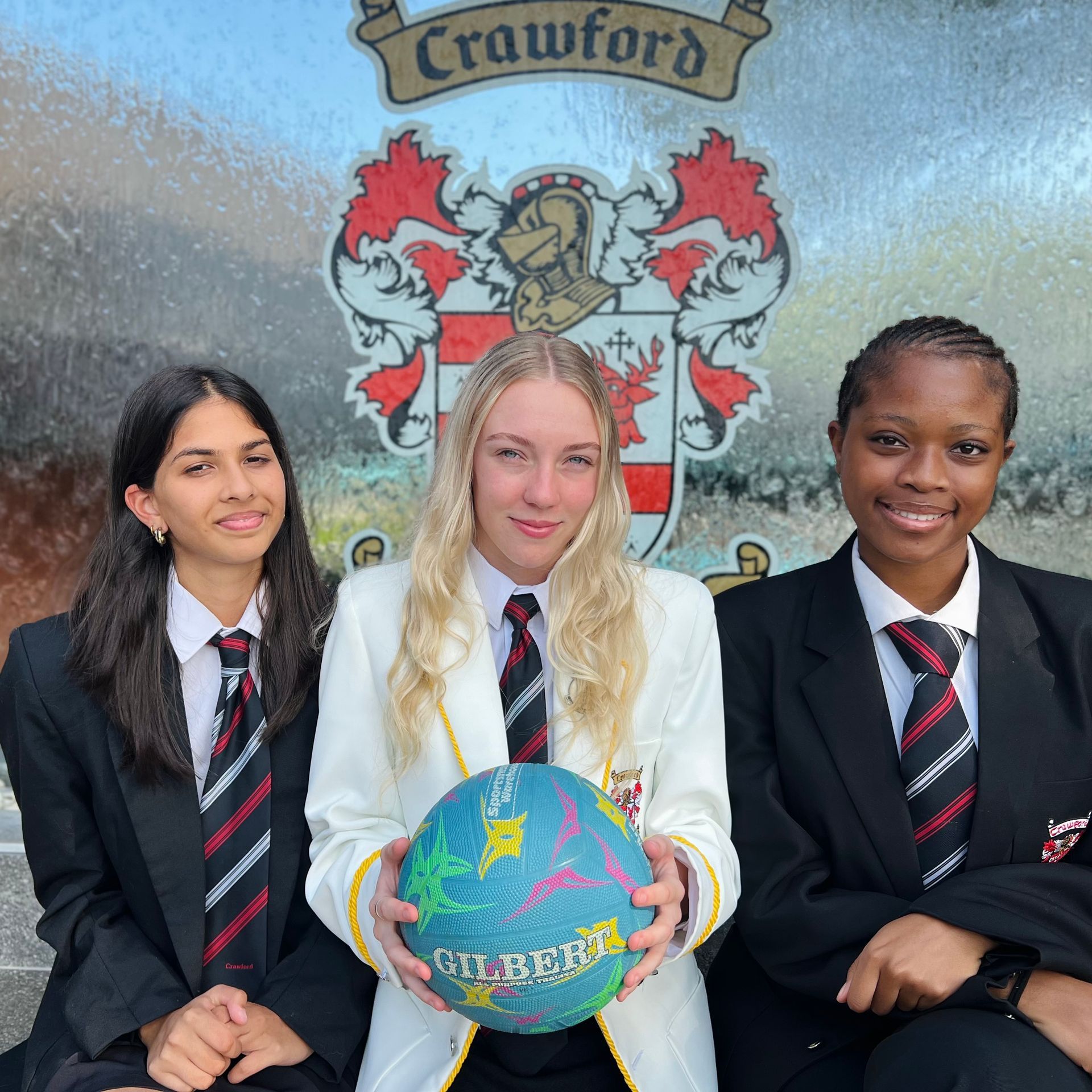 Three girls are posing for a picture in front of a crawford coat of arms