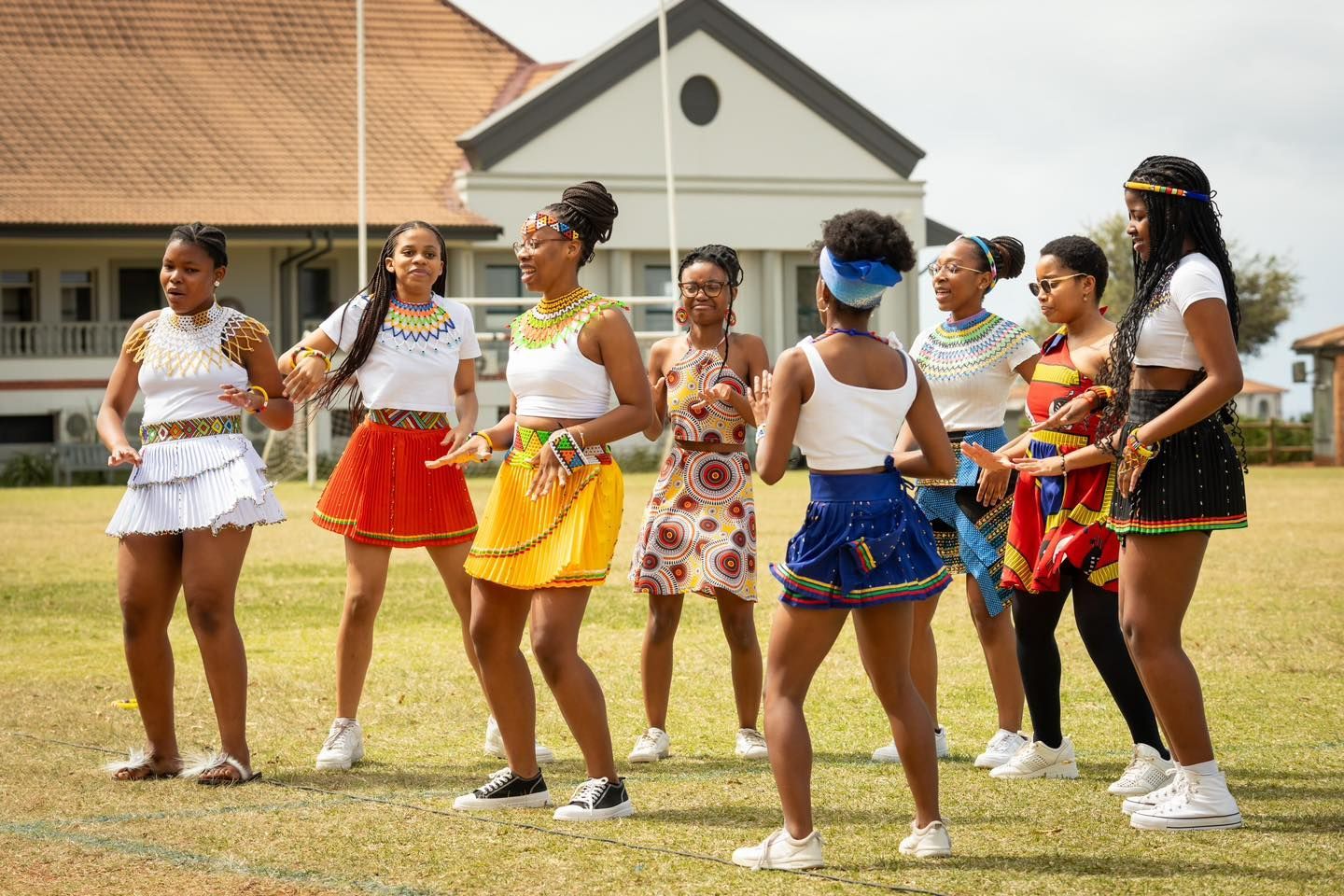 A group of young women are dancing in a field in front of a building.