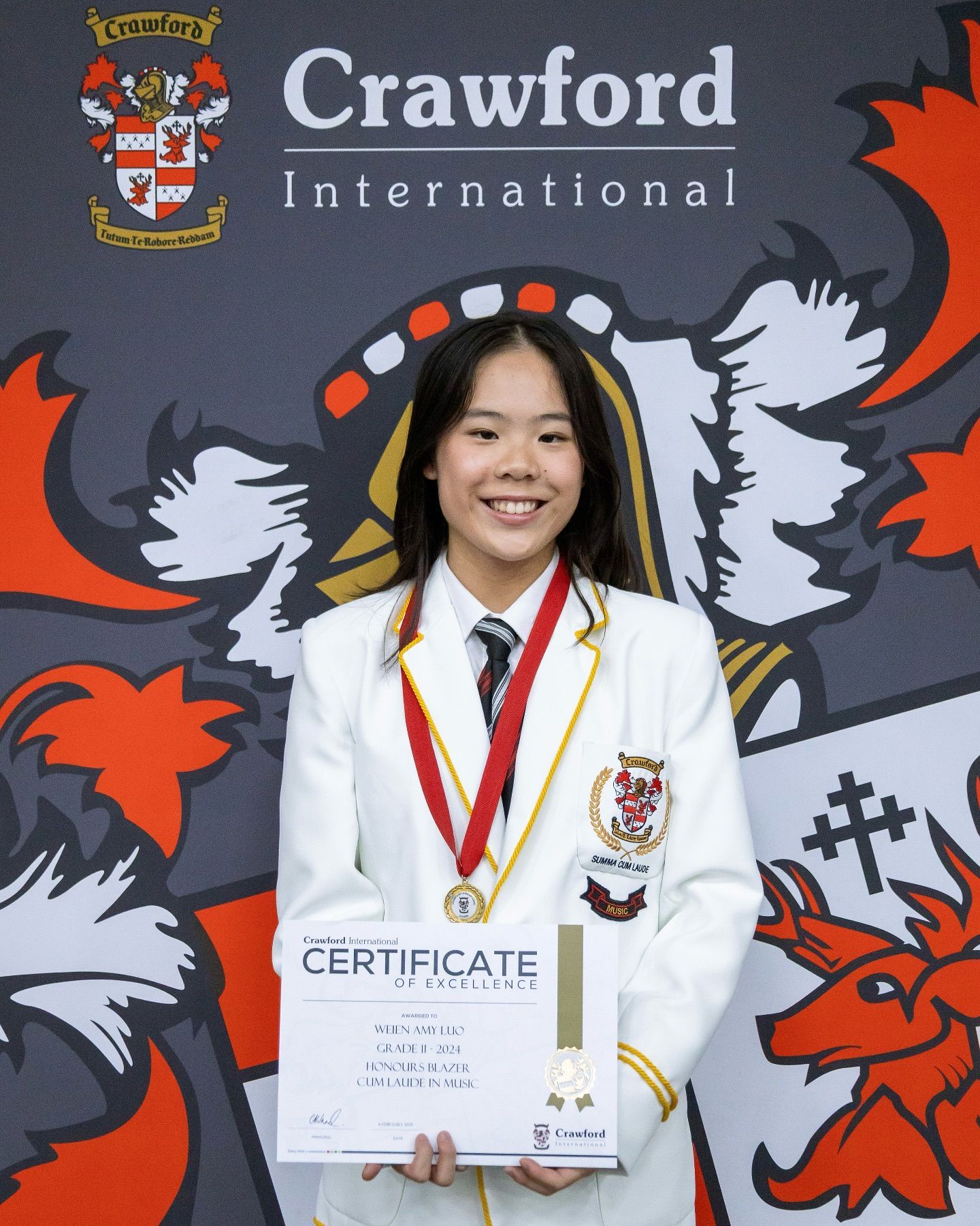 Young woman in uniform holding certificate, smiling, in front of Crawford International school logo.