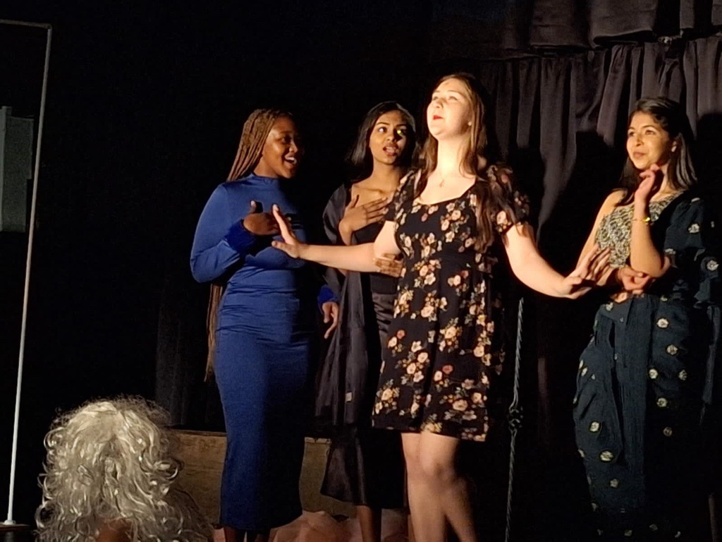A group of women are standing on a stage in a dark room.