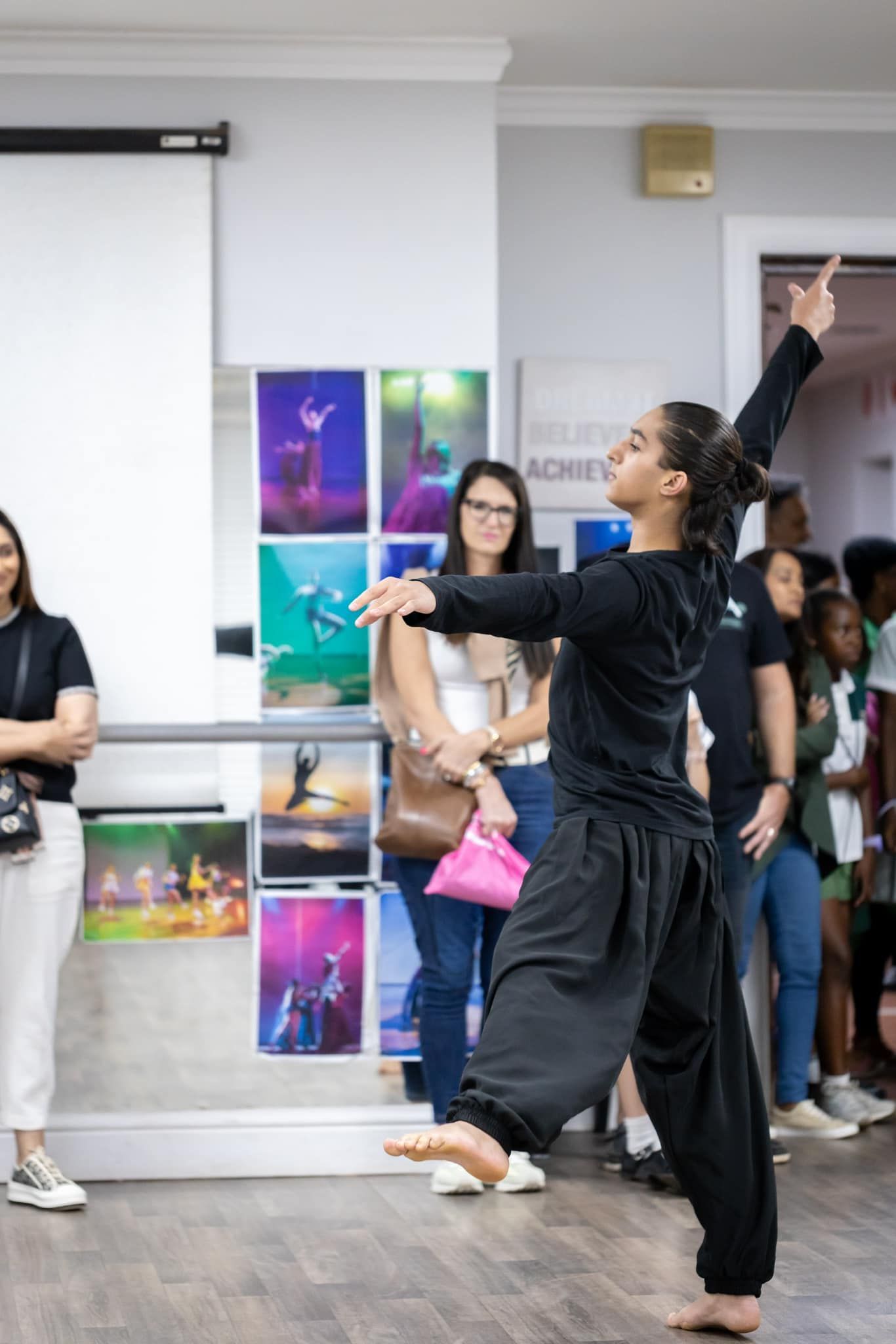 Dancer performing, wearing black clothing, in front of an audience and artwork.