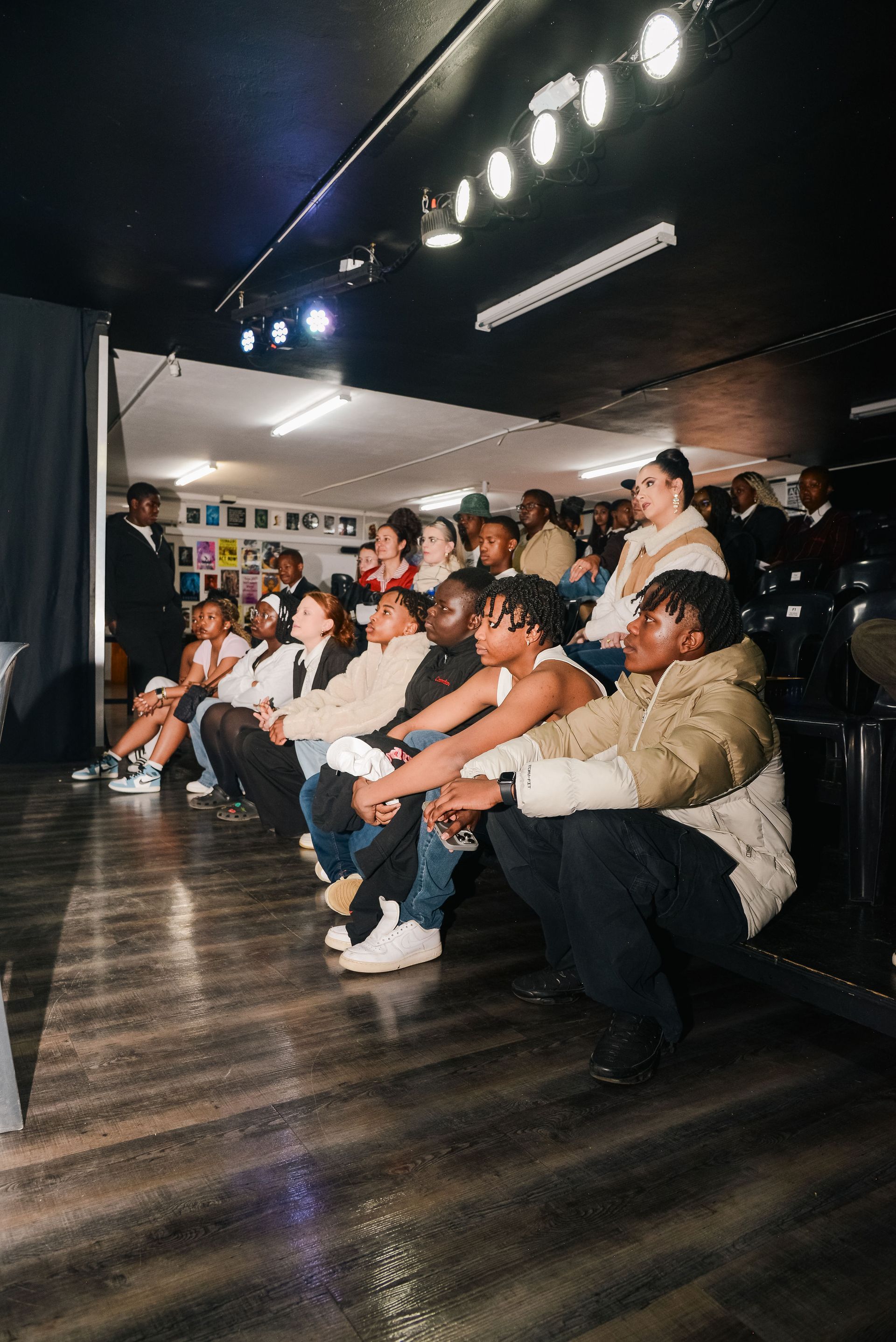 People seated, watching a performance in a dimly lit space.