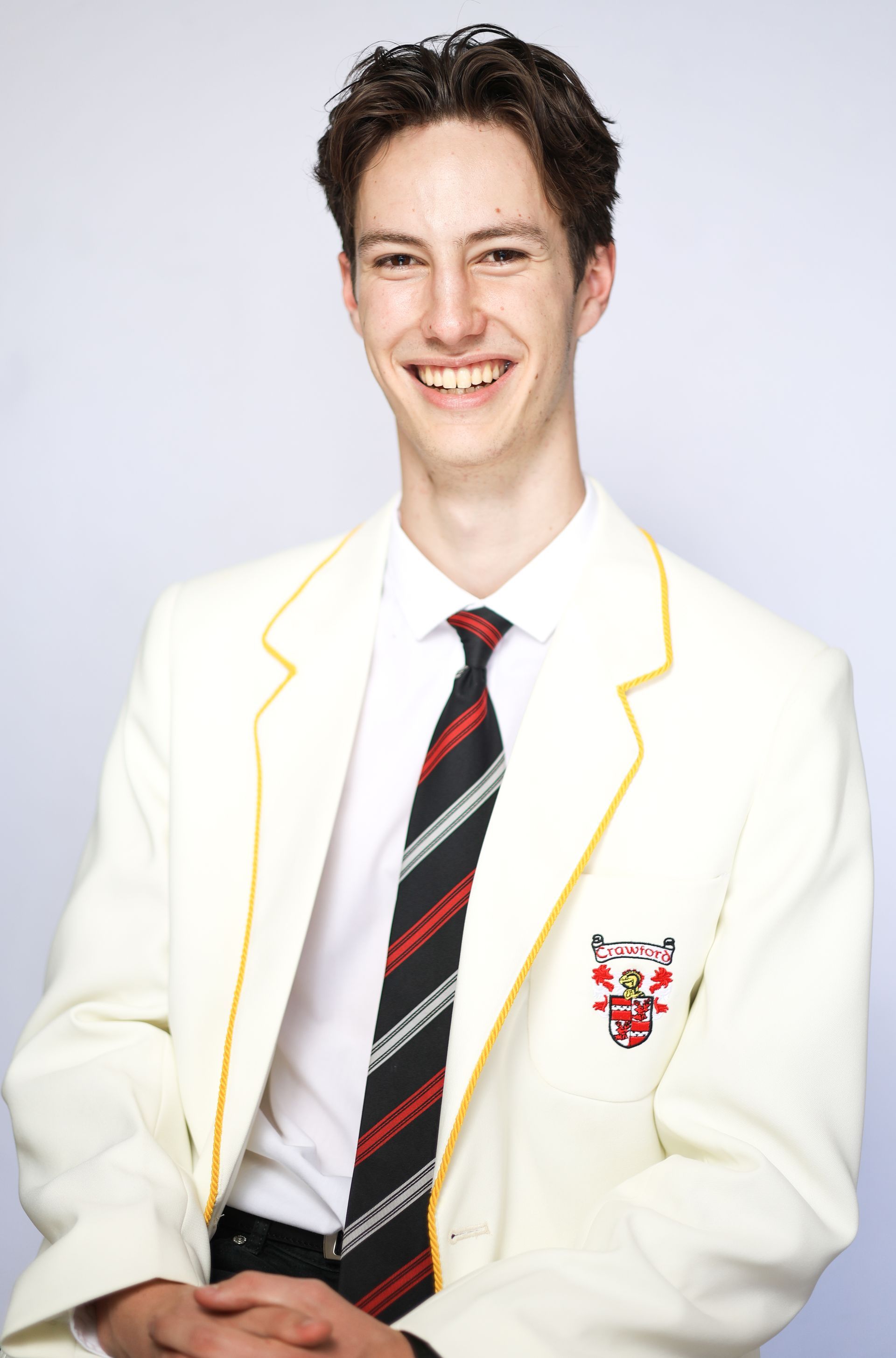 A young man wearing a white jacket and tie is smiling for the camera.