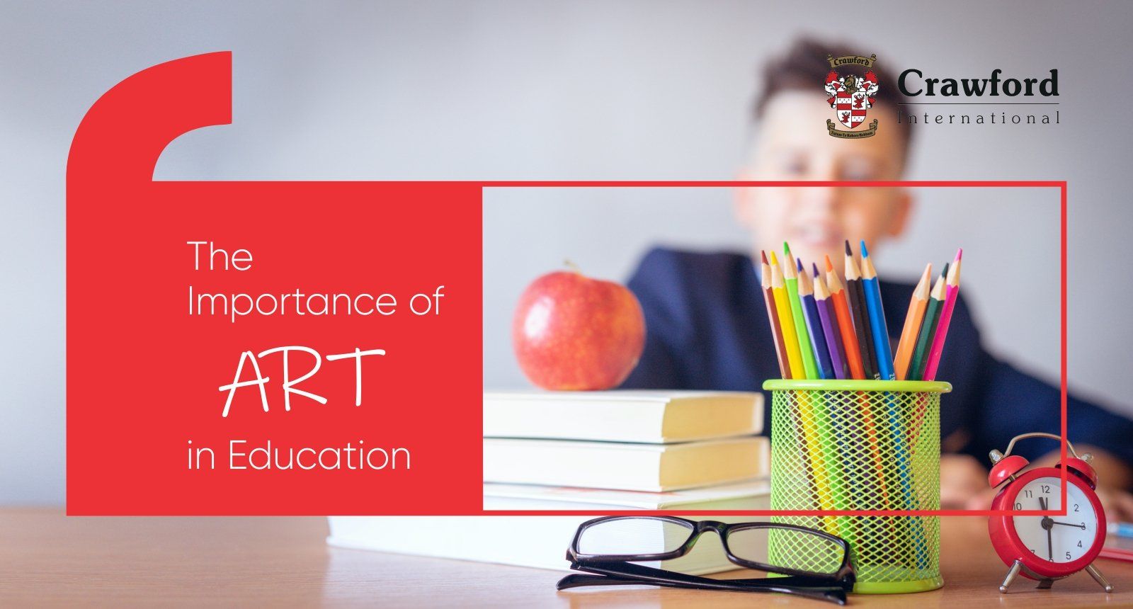 A boy is sitting at a desk with books , pencils , glasses and an apple.
