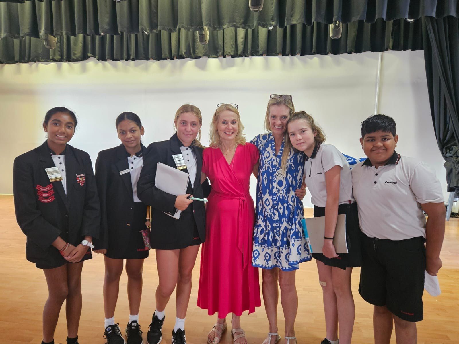 A group of young girls are posing for a picture with a woman in a red dress.