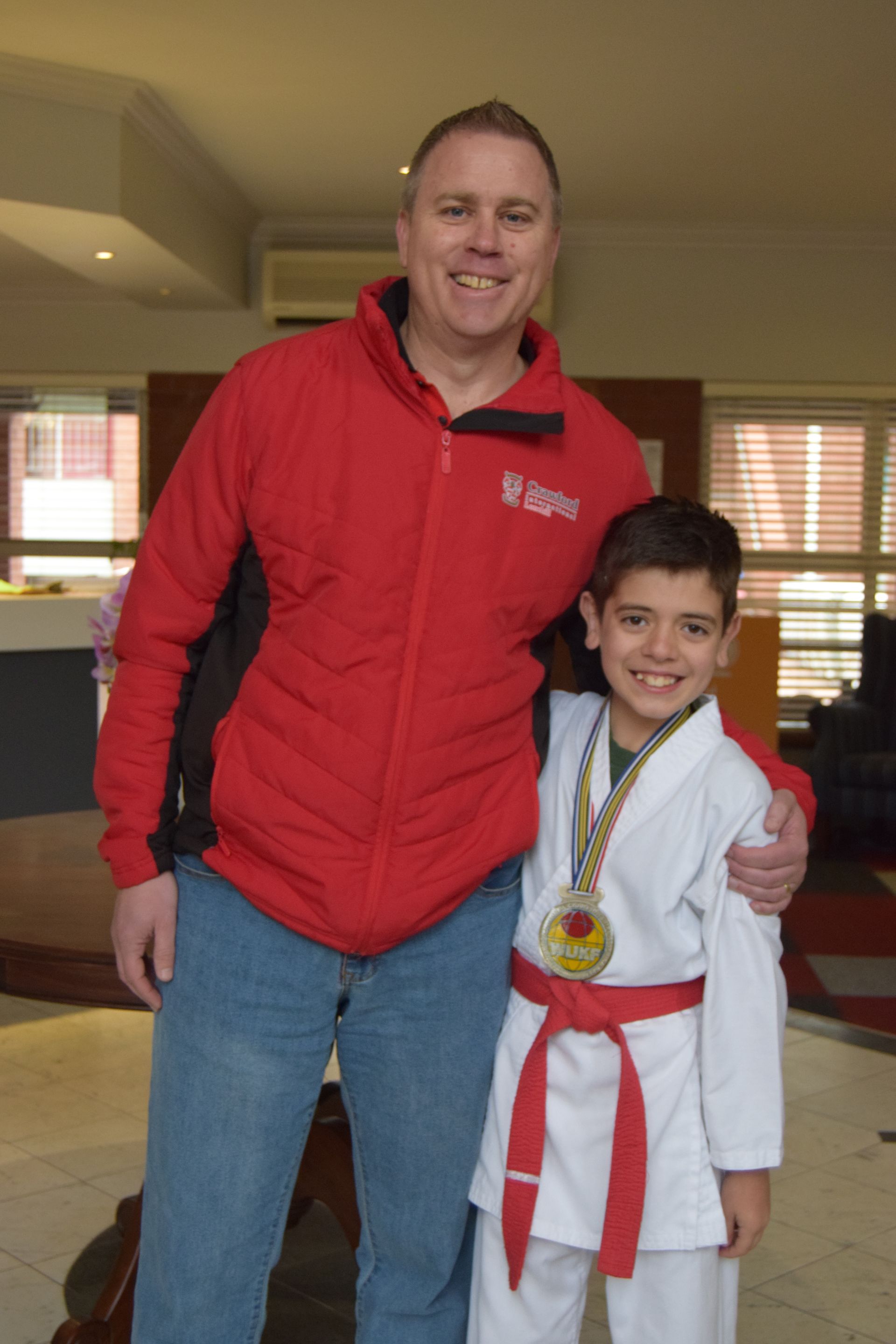 A man in a red jacket stands next to a boy in a white karate uniform